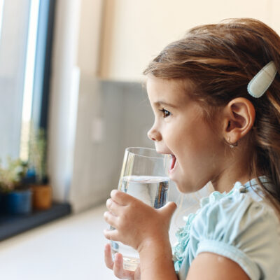 Little girl drinking water from the glass in the kitchen.